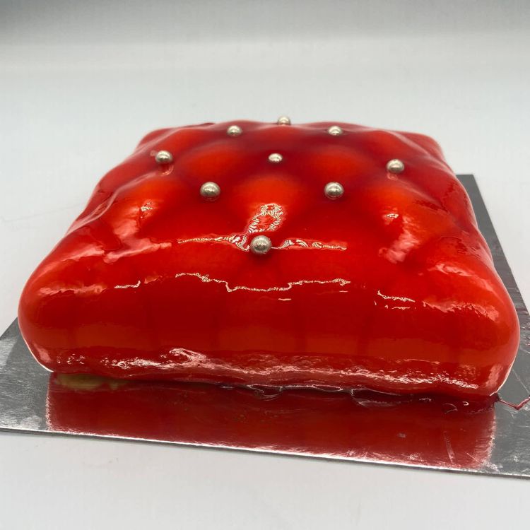 Imagen tarta de color rojo con forma de cojín y botones plateados todo muy brillante 